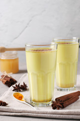 Ayurvedic golden turmeric latte milk in two glasses with curcuma powder, cinnamon and anise star on gray concrete background, Vertical format