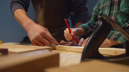Boy with pencil makes serifs on a wooden board. Garage workshop