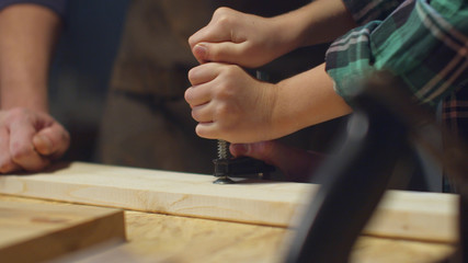 The boy tries to clamp a wooden board in a vice