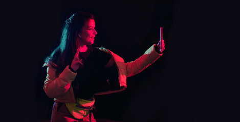 Tik tok advertisement concept.Young girl posing with smart phone in her hands, making selfie on black background.TIK TOK is a popular social network on the internet.Studio shots, copy space for text