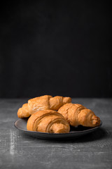 Side view on sweet croissants on a plate on the dark grey background, vertical format