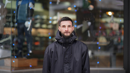 Young impressive man with black beard a black jacket on the street on window