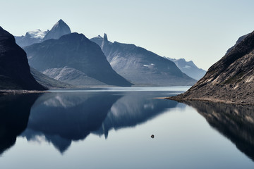 Landscape photo with mountains reflecting in the  fjord with a small boat 
