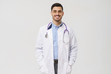 Horizontal portrait of handsome man physician, isolated on gray background with stethoscope around neck, showing confident smile, ready to help patients with health problems