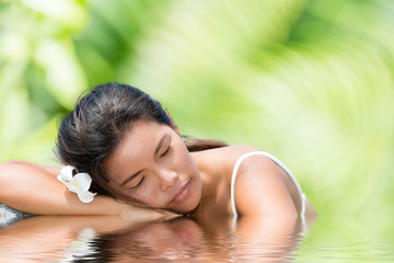 Obraz na płótnie Canvas Beautiful asian girl with frangipani flower in the hair resting outdoors at the infinity pool.Copy space