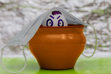 Easter composition. Under a medical face mask, a chicken egg in a clay pot on a silver background....