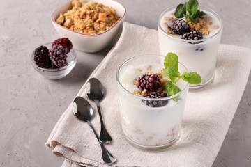 Two servings of homemade natural yogurt with granola, blackberries and mint in glasses on a gray background, Diet and weight loss control concept, Space for text, Closeup