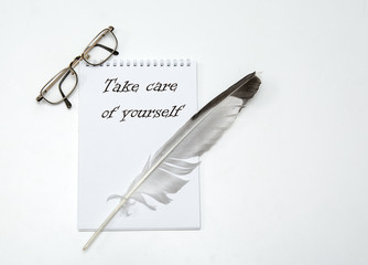 On a white background lies a notebook. Top left are vintage glasses. On the notebook is a goose quill. And the inscription - take care of yourself. Concept - protect your health