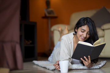 woman lying down reading with cup of coffee in pandemic house, coronavirus quarantine in mexico