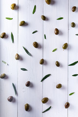 group of olives scattered on a white table with some leaves in an overhead view