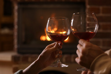 Lovely couple with glasses of wine near fireplace indoors, closeup. Winter vacation