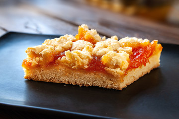 Homemade apricot pie. Slice of rustic hot sweet pie on a black plate on a wooden background. Natural organic food. Selective soft focus.