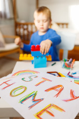 Fototapeta premium Stay at home. Children's drawing with on a white sheet. Child on back play in soft focuse .Campaign on social networks for the prevention of coronavirus