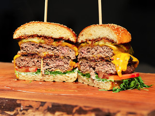 A Big selfmade Burger on a wooden plank cutted in two halfes