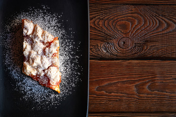 Homemade apricot pie. Top view slice of rustic hot sweet cake sprinkle with powdered sugar in black plate on a wooden background. Natural organic food. Selective soft focus. Copy space.