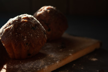 fresh muffins with chocolate lie on a wooden board sprinkled with icing sugar, top view.
