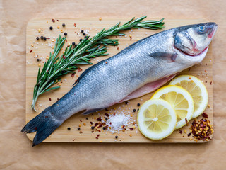 Raw uncooked sea fish preparation - seabass choice of fish on cutting board on the parchment paper. Mediterranean seafood concept. Top view with copy space.
