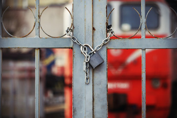 Locked padlock hanging on chain on closed gate to railway
