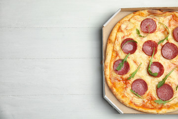 Tasty pepperoni pizza in cardboard box on white wooden table, top view. Space for text