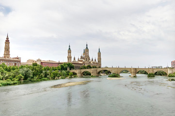 View of the Cathedral-Basilica of Our Lady of the Pillar, a Roman Catholic church on river Ebro and the Old Stone bridge in the city of Zaragoza, in Aragon, Spain.