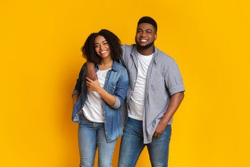 Smiling black man posing with girlfriend over yellow background in studio