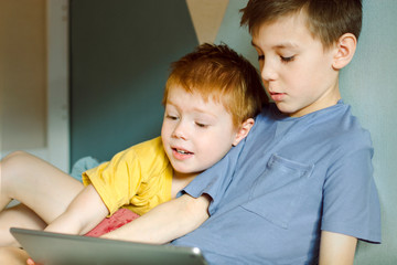 two boys aged 10 and 4 study something on a computer tablet together in close-up