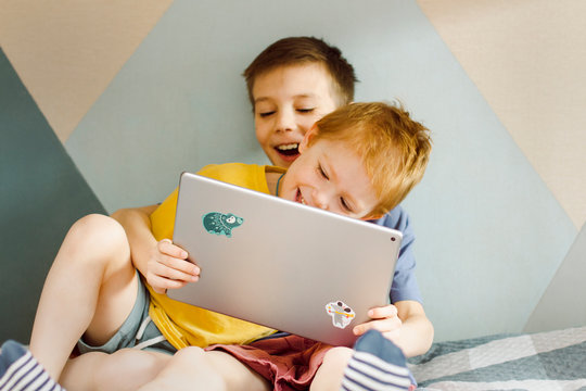 two children are sitting at home looking at a computer tablet and laughing