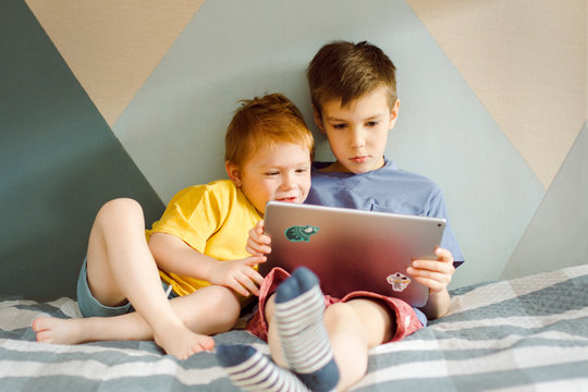two boys in yellow and blue t-shirts sit and look at a computer tablet