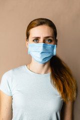 Portrait of a red-haired girl in a medical mask on a beige background, virus protection.