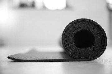 The yoga mat folded into a roll lies on the floor. Black and white photo