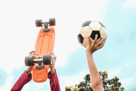 Cropped Hands Of Children Holding Soccer Ball And Skateboard Against Sky