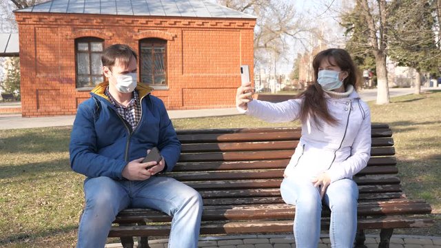 Coronavirus protection. woman and man in medical protective mask are sitting with smartphone on city street in Europe. Tourists on street wear a protective mask from viruses selfies on smartphone.