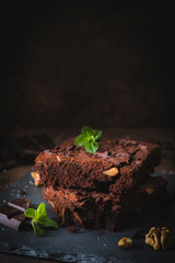 Pieces of walnut brownies with dark chocolate and mint leaves on a slate platter and dark brown...