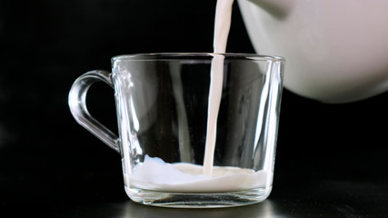 Cold milk is poured into a glasson black background. Close up.