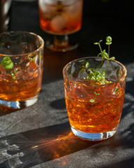 orange summer cocktail with ice on dark background. Shadows of glasses, hard sun light.