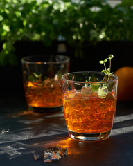 orange summer cocktail with ice on dark background. Shadows of glasses, hard sun light.