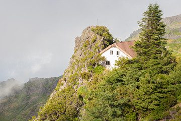 A white house with a tiled roof in the mountains among the clouds.