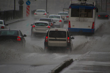 cars driving in heavy rain on a road sprinkling puddles in all directions