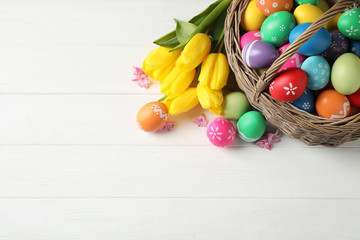 Obraz na płótnie Canvas Colorful Easter eggs and flowers on white wooden background, flat lay. Space for text