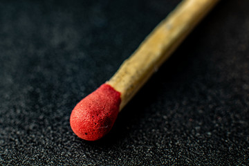Red match head on dark, rough background. Macro photography. 