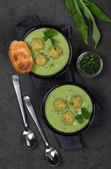 Cream soup of greens with meatballs with croutons in a bowl on a dark background top view