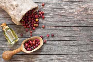 Glass bottle of juniper essential oil with dried juniper berries in wooden spoon on rustic table (juniperus)