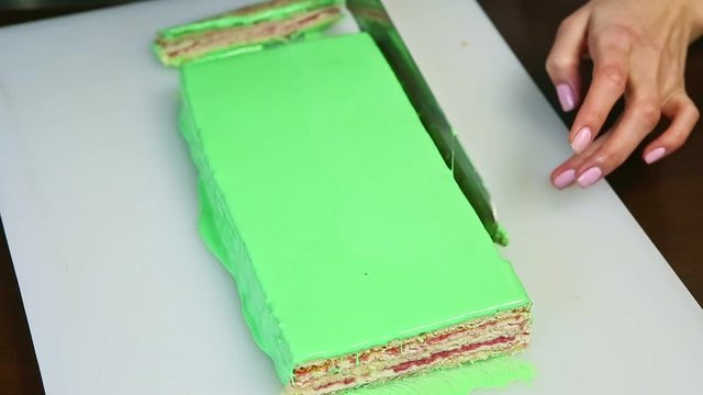 top view on hands cutting off by knife one edge of green glazed creamy layered cake