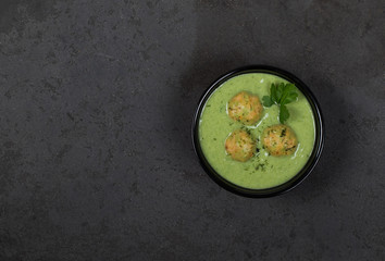 Cream soup of greens with meatballs in a bowl on a dark background top view