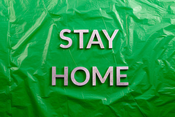 the words stay home laid with silver metal letters on crumpled green plastic background in flat lay...