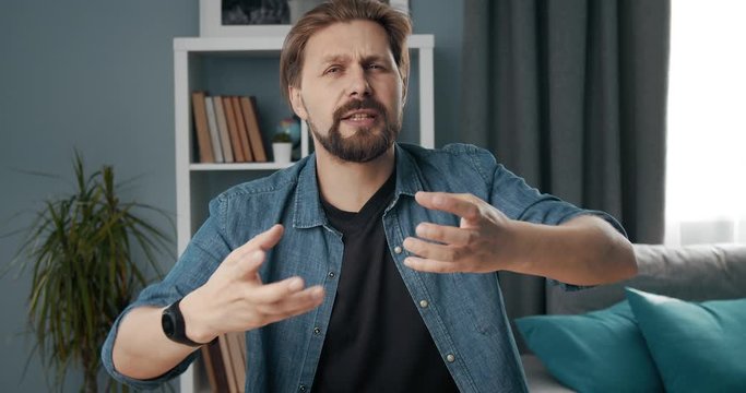 First person view of mature businessman in domestic outfit talking and gesturing emotionally during video conference on laptop. Bearded man working remotely and having online conversation.