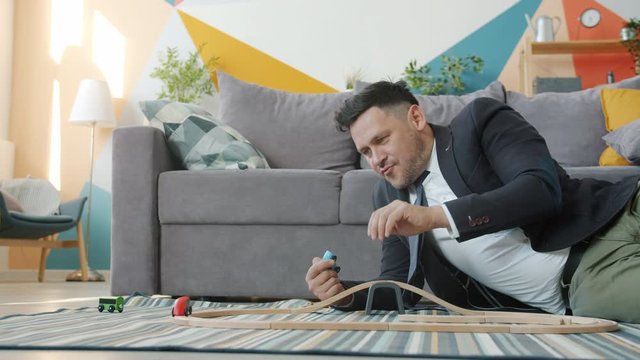 Slow motion of handsome guy in formal clothing playing with toy cars at home enjoying carefree game having fun alone. Businessmen and relaxation concept.