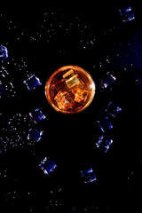 Whiskey with ice cubes on black background from above.Glass of scotch and ice cubes on a on black background