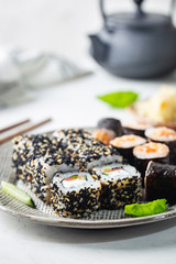 Set of sushi and maki on plate with soy sauce and chopsticks on white background. Top view with copy space