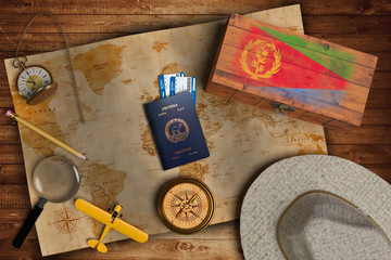 Top view of traveling gadgets, vintage map, magnify glass, hat and airplane model on the wood table background. On center, official passport of Eritrea and your flag.